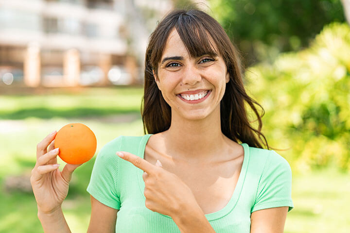 Una chica muestra una naranja y explica los beneficios de comer naranjas y clementinas